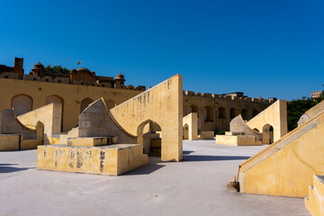 the unique astronomical instruments at Jaipur’s Jantar Mantar observatory. The geometric structures, made of yellow sandstone, feature arches and curves under a bright sunlit sky.
