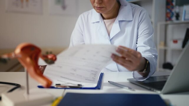 Female obstetrician looking at ultrasound image and typing on laptop in clinic