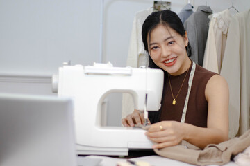 Asian woman using at a sewing machine. She has a tape measure draped around her neck.