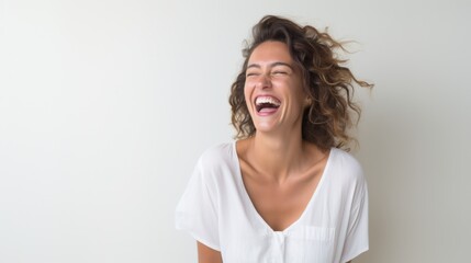 A person wearing a white shirt is laughing heartily against a light background, radiating joy and infectious happiness.