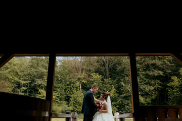 A bride and groom are standing in front of a barn, with the bride holding a bouquet