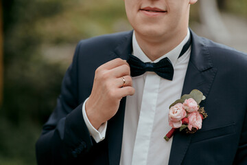 A man in a suit and tie is getting ready for a wedding. He is adjusting his tie and putting on a boutonniere