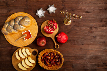 Challah, honey, apple and pomegranate and burning candles on the table with a menorah Rosh Hashanah...
