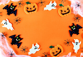 Halloween frame with pumpkin, bat, spider web and ghost party decorations on orange background, top view. Copy space.