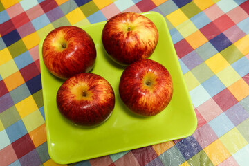 close up of four red fresh apples on a green plate on a colourful table cloth