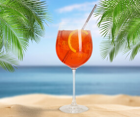 Summer beach with delicious Aperol Spritz cocktail, palm leaves and golden sand