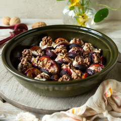ceramic dish with baked plums with ricotta and walnuts on light table