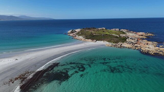 Small island with a sandbar with blue sea and turquoise waters, aerial shot rearward
