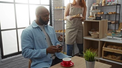Man using phone in bakery while waitress serves pastries in cozy cafe interior