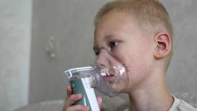 A young boy undergoes inhalation therapy at home to prevent asthma complications and colds. He uses a nebulizer while sitting comfortably in a cozy environment.