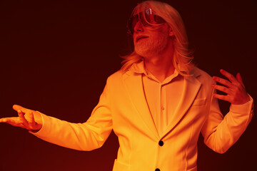 Stylish man with long hair in a white suit expressing confidence against a warm orange background,...