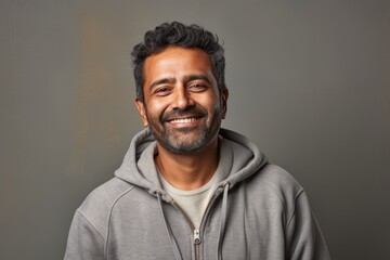 Fototapeta premium Portrait of a smiling indian man in his 50s wearing a zip-up fleece hoodie on bare concrete or plaster wall