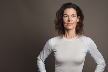 Obraz premium Portrait of a glad woman in her 40s showing off a lightweight base layer in blank studio backdrop