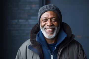 Portrait of a grinning afro-american man in his 60s wearing a warm parka in front of blank studio backdrop