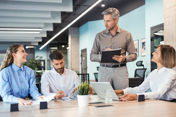 Young handsome man gesturing and discussing something while his coworkers listening to him sitting at the office table.