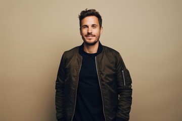 Obraz premium Portrait of a blissful man in his 30s wearing a trendy bomber jacket isolated on light wood minimalistic setup