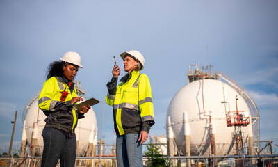 Fototapeta premium Engineers wearing safety gear, including hard hats examining survey a large blueprint tablet standing industrial facility gas or oil refinery engaged in a job requires high safety standards concept