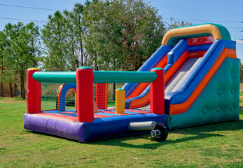 A colorful inflatable slide features for kids on the green grass with trees on background