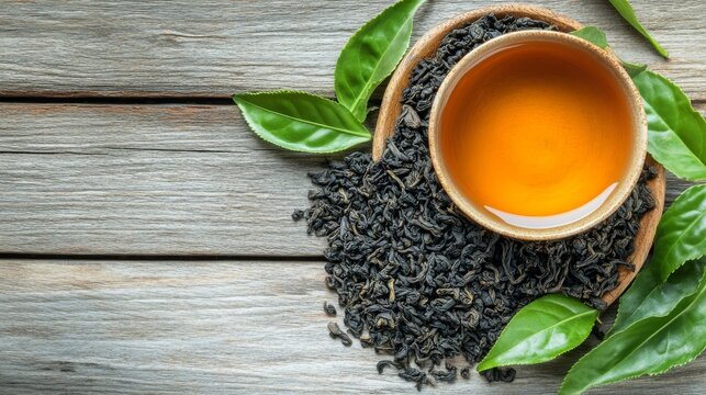Taza de t&eacute; caliente rodeada de hojas de t&eacute; y hojas frescas sobre una superficie de madera. La imagen resalta la frescura y pureza del t&eacute;, ideal para representar conceptos de naturaleza y bienestar.