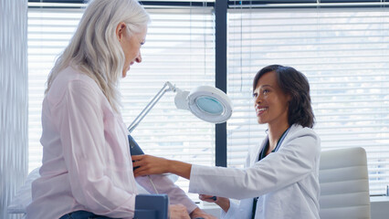 Obraz premium Mature Woman Patient Having Blood Pressure Taken By Female Doctor In Office