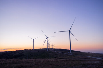 Silhouette of wind turbines against a colorful sunset sky. The gentle fading light highlights the...