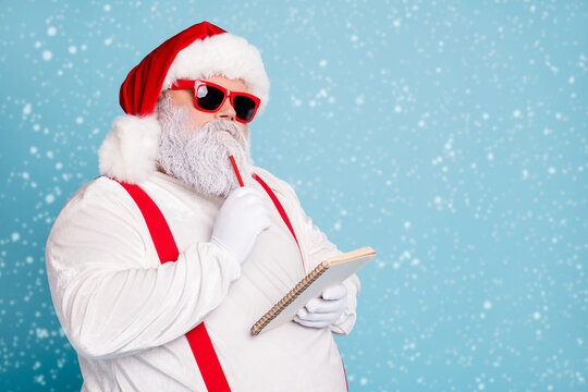 Close up photo of focused funny funky fat santa claus hold notebook think about wish list plan decide what choose look thoughtful wear stylish trendy suspenders isolated over blue color background - Powered by Adobe