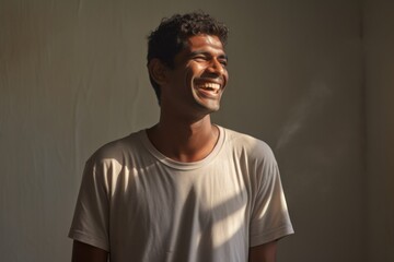 Fototapeta premium Portrait of a grinning indian man in his 20s sporting a long-sleeved thermal undershirt isolated in bare monochromatic room