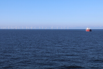 seascape with a line of offshore wind mills on the horizon and a large cargo ship in the distance