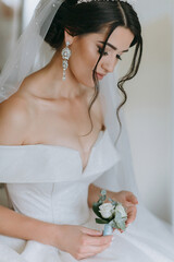 A woman wearing a white dress and a veil with a flower in her hand. She is wearing a pair of...