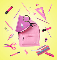 Pink backpack and school stationery in air on yellow background
