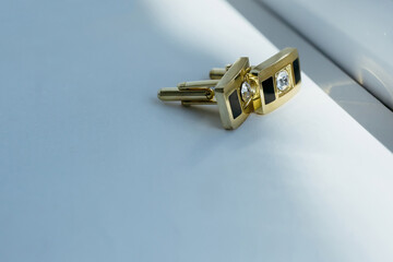 A pair of cufflinks with a diamond and black design sit on a white table. The cufflinks are made of...