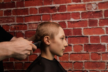 Teenager gets a short haircut with a hair clipper  A male barber gives a haircut with a clipper, to a teenage boy