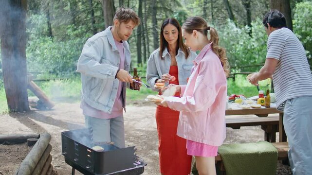 Relaxed friends preparing burgers at forest picnic. Group assembling sandwiches