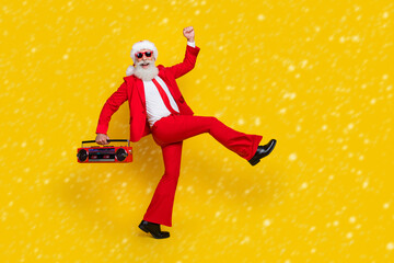 Full length photo of funky cool santa dressed red suit tie enjoying boom box songs walking empty space isolated yellow color background © deagreez