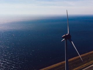 Aerial view of windmill turbine with rotating propeller standing in area of coastline and farmland...