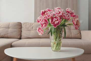 Vase of pink tulips on coffee table with blurred background of beige modern cozy light living room.  Copy space