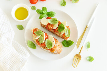 Bruschetta toasts with mozzarella, cherry tomato and basil leaves on white wooden table