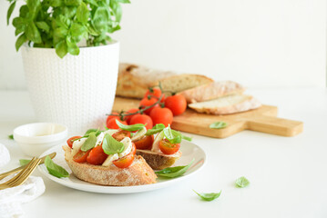 Bruschetta toasts with mozzarella, cherry tomato and basil leaves on white wooden table