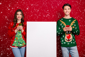 Portrait of two beautiful positive partners hold telephone empty space eshop promo poster isolated on red color background