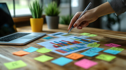 Obraz premium An elegant hand is pointing at chart on a rustic wooden table, Colorful sticky notes 