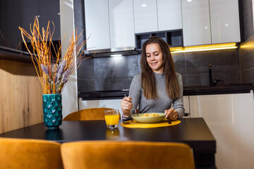 Woman eating mac and cheese in her apartmen. Drinks orange juice.