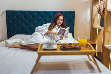 Pretty girl in the hotel room with bathrobe chilling and reading a book.