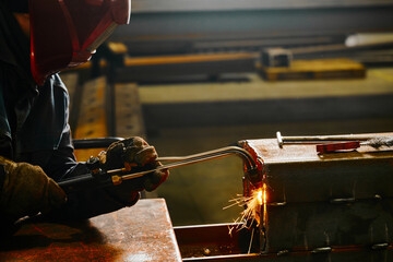Welder in mask cuts steel beam with cutting blowpipe in shop