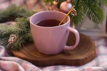 A cup of hot tea on a wooden stand with a Christmas spoon. Christmas tree with Christmas tree toys