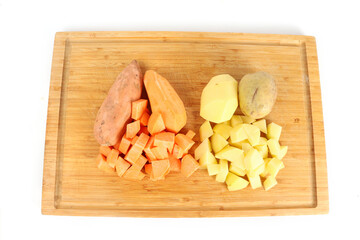 sweet potatoes and potatoes cut up on a wooden chopping board  
