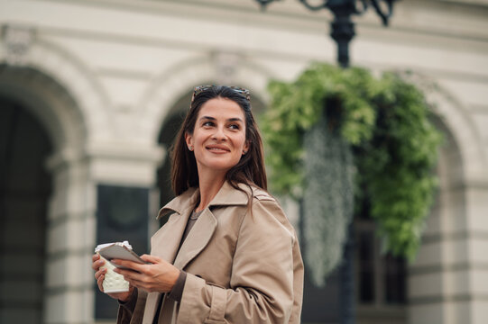Smiling businesswoman walking in the city and using smartphone