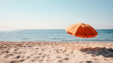 A serene beach scene featuring an orange umbrella in the sand against a clear blue sky, evoking a sense of relaxation and leisurely vacation moments by the sea.