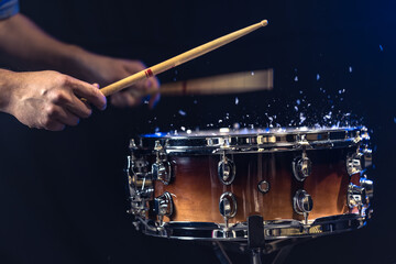 Drum sticks hitting snare drum with splashing water on black background.