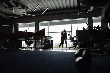 Silhouette of a man and a woman hugging and standing near a panoramic window. Men and women flirt in the workplace. Romantic kisses in the office.