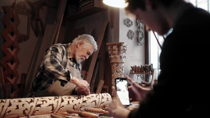 Young boy off focus recording grandfather or teacher with smartphone. Recording video or making photos of older man working as carpenter. Concept of modern technology. Joiner creating ornament. - Powered by Adobe